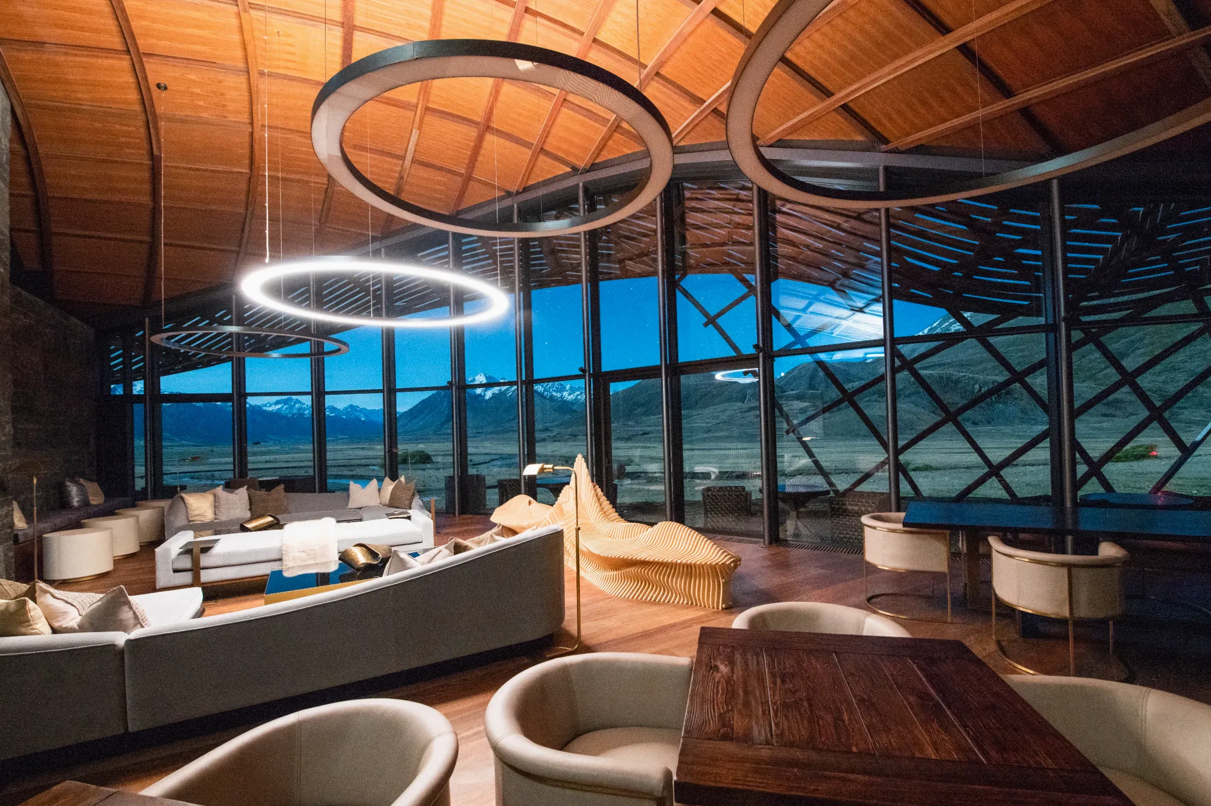 Restaurant interior at evening with warm lighting, set tables and view of the alpine garden